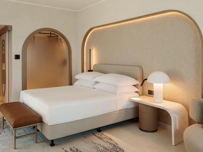 Modernes Schlafzimmer mit großem Bett, abgerundetem Wanddesign und warmem LED-Licht.