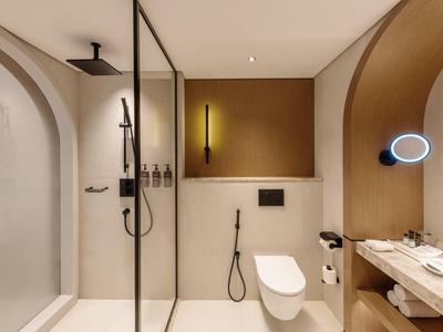 Moderner Badezimmerspiegel mit runder Beleuchtung, weiße Toilette, offene Dusche und braune Wandakzente.