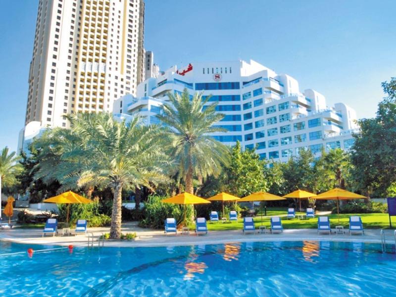 Moderner Wolkenkratzer und Hotel neben einem Pool mit Palmen und Sonnenschirmen.