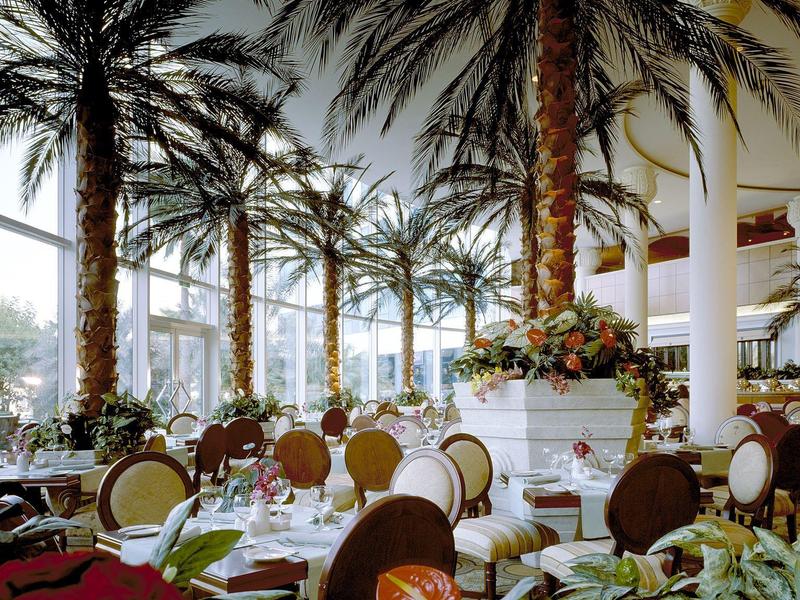 Eleganter Hotel-Speisesaal mit Palmen, gedeckten Tischen und Blumendekoration.