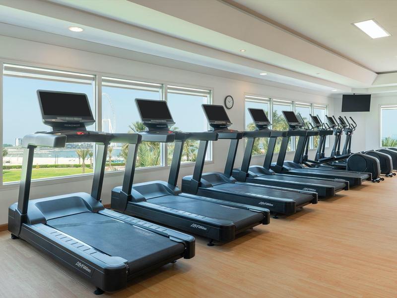 Mehrere Laufbänder in einem hellen Fitnessraum mit großen Fenstern und Holzboden.