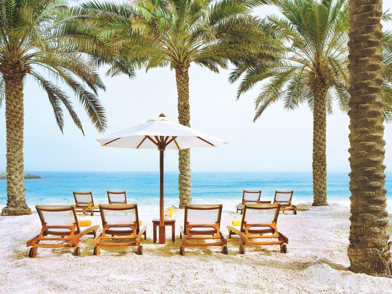 Strand mit Liegestühlen, Sonnenschirm und Palmen vor klarem blauem Meer