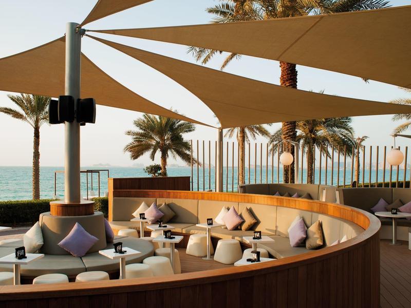 Outdoor-Loungebereich mit runden Holzmöbeln und Sonnensegeln am Meer