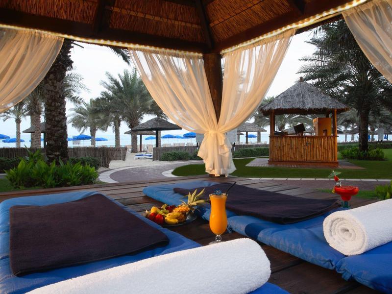 Entspannender Pavillon mit Kissen, Handtüchern und Getränken, umgeben von Palmen am Strand.