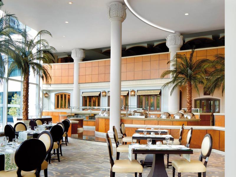 Elegantes Restaurant mit weißen Säulen, Palmen und stilvollen Sitzgelegenheiten in hellem Interieur.