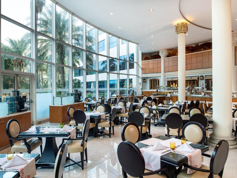 Helles Hotelrestaurant mit großen Fenstern, runden Tischen und eleganten Stühlen.