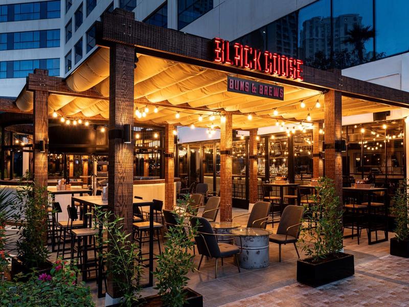 Beleuchtete Außenterrasse eines Restaurants in einem städtischen Hotel mit Sitzgelegenheiten und Pflanzen.