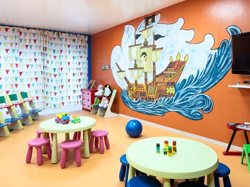 Bunter Kinderspielraum mit Tischen, Stühlen und einer Piratenschiff-Wandmalerei.