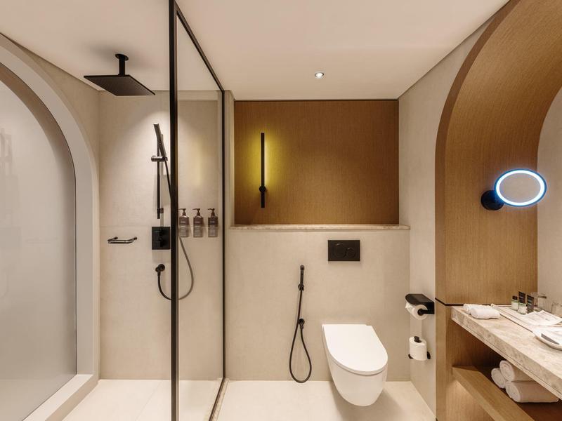 Modernes Hotelbad mit Regendusche, wandhängendem WC und großem Spiegel mit beleuchtetem Make-up-Spiegel.
