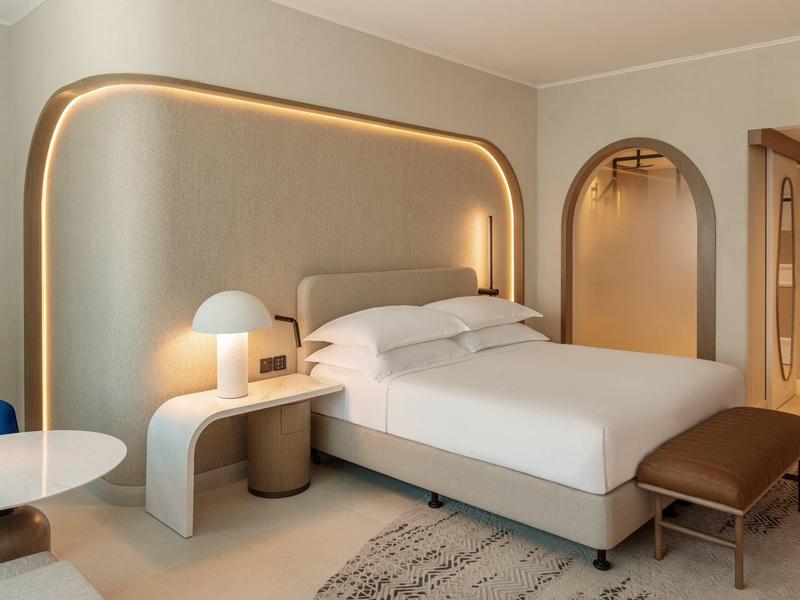 Modernes Hotelzimmer mit großem Bett, weichen Farben und dekorativer Beleuchtung an der Wand.