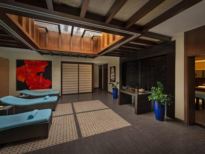 Innenraum mit Holzbalkendecke, blauen Liegen, großen Teppichen, Pflanzen in blauen Töpfen, Kunst an Wand.