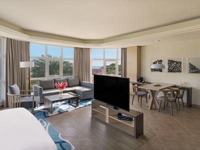 Modernes, helles Hotelzimmer mit Panoramafenstern, Sitzbereich und Esstisch.