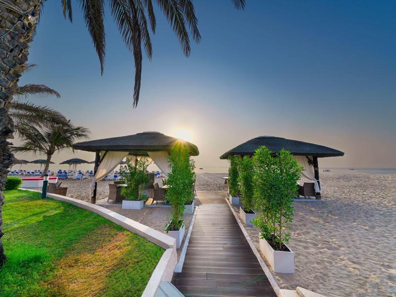 Strandweg mit grünen Pflanzen, Palmen und zwei schattigen Pavillons bei Sonnenaufgang.