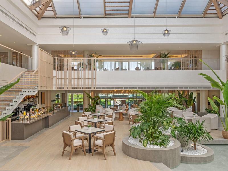 Heller, moderner Innenraum mit Pflanzen, runden Tischen, Holzstühlen und großer Glasdecke.