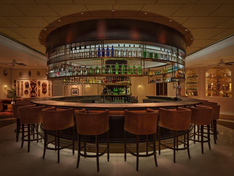 Gemütliche Bar mit braunen Ledersesseln und runder Theke, warm beleuchtet und mit Flaschenregalen.