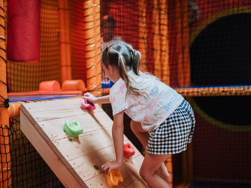 Kind spielt Tischtennis in buntem Indoor-Spielplatz mit weichem Geländer und Kletternetz.