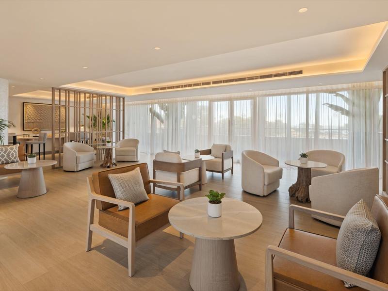 Helles, modernes Wohnzimmer mit Holzmöbeln, beigen Sesseln und großen Fenstern mit transparenter Gardine.