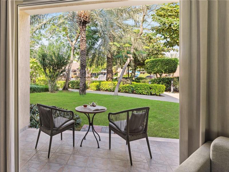 Zwei Stühle und ein kleiner Tisch auf einer Terrasse mit Blick auf einen grünen Garten.