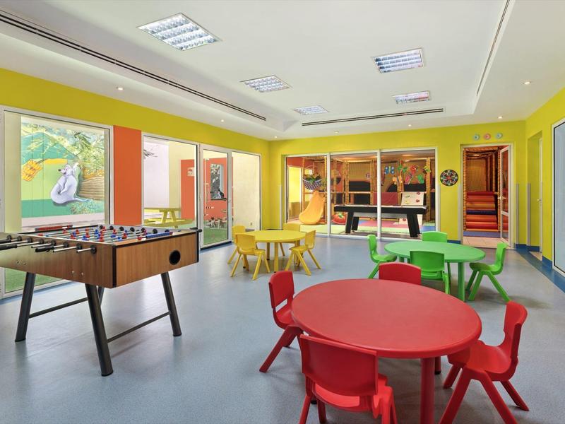 Bunter Spielraum mit Tischen, Stühlen und einem Kicker in gelbem, lichtdurchflutetem Raum.