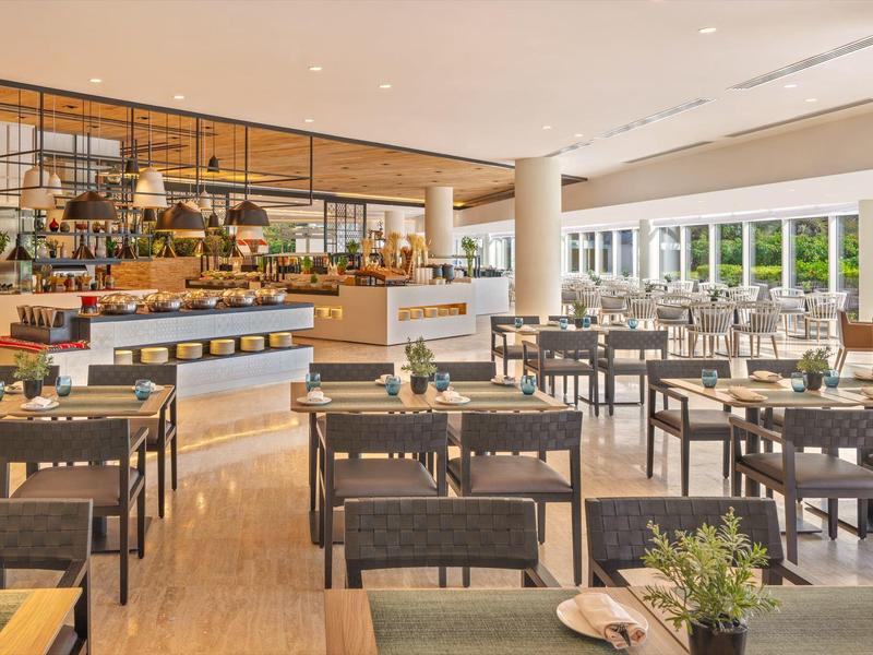 Moderner, heller Speisesaal mit braunen Tischen, Stühlen und großem Fenster zur Terrasse.