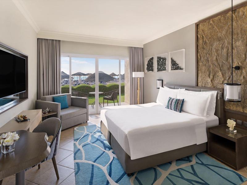 Modernes Hotelzimmer mit großem Bett, Sitzbereich, TV, Balkon und bergiger Aussicht.