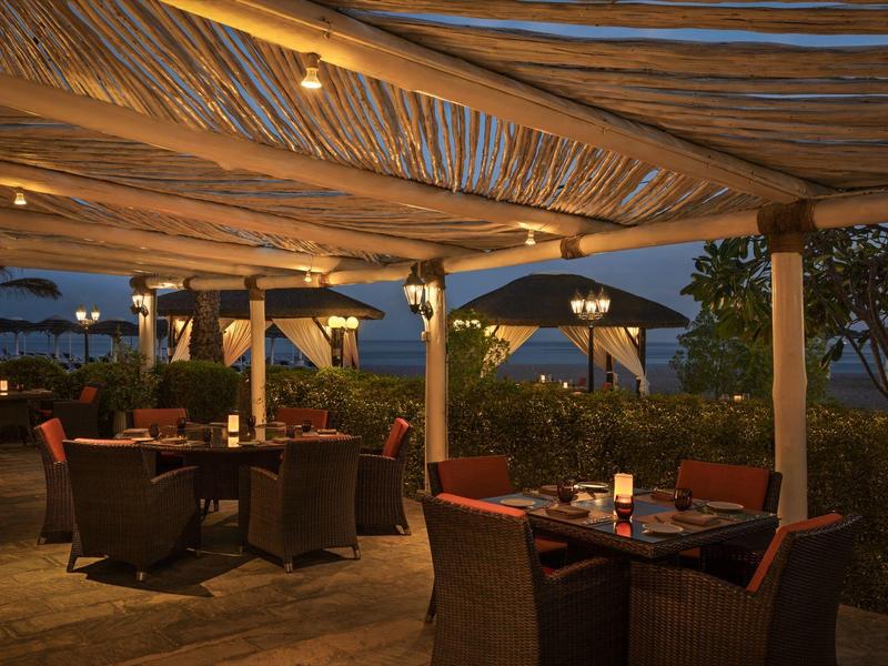 Gemütliche Außenterrasse mit gedeckten Tischen, Stühlen und warmem Lampenlicht bei Abenddämmerung.