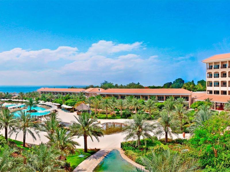 Großer Hotelkomplex mit Pool, Palmen und Blick aufs blaue Meer unter klarem Himmel.