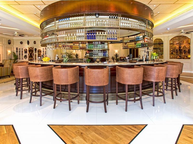 Moderner, runder Barbereich mit Lederhockern, beleuchtetem Deckenspiegel und Holzfußboden.