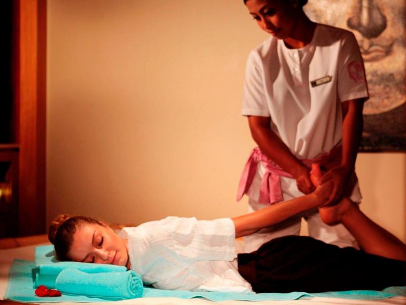 Eine Frau erhält Fußmassage auf Bambusliege, Hintergrund mit großer Buddha-Bildwand.