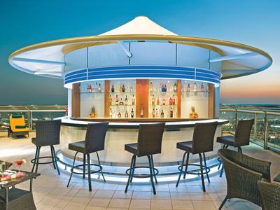 Moderner runder Rooftop-Barbereich mit Sitzgelegenheiten und Blick auf die Stadt bei Sonnenuntergang