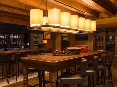 Rustikaler Barbereich mit Holztheke, Sitzhockern und warmen Pendelleuchten im Hotel.