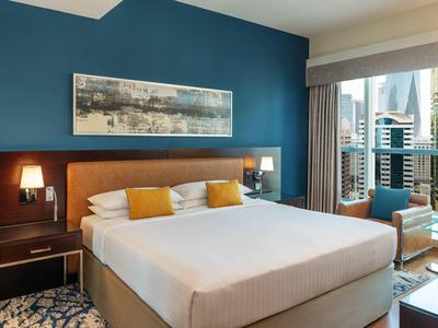 Modern eingerichtetes Hotelzimmer mit großem Bett, blauer Wand und Stadtblick vom Balkon.