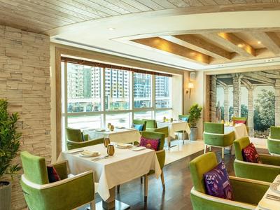 Eleganter Speisesaal mit grünen Sesseln und großen Fenstern mit Blick auf Hochhäuser.