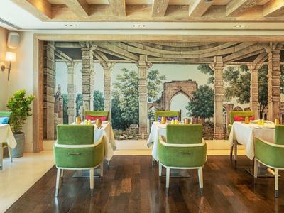 Helles Restaurant mit grünen Stühlen, weißen Tischdecken und Wandbild mit Naturmotiven.