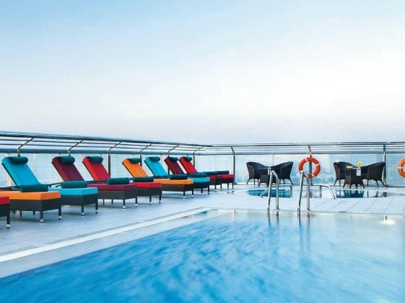 Heller Außenschwimmbadbereich mit bunten Liegen und Blick auf das ruhige Meer unter blauem Himmel.