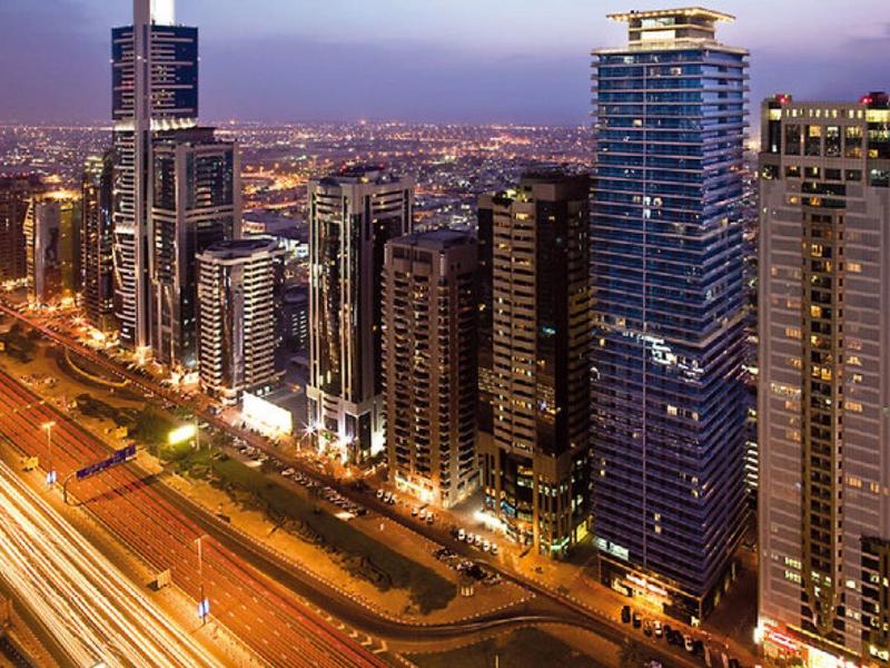 Blick auf eine belebte Stadtstraße mit Hochhäusern und beleuchteten Autos bei Abenddämmerung.