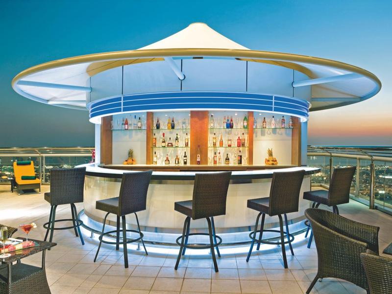 Moderne Dachbar mit runden weißen Sonnenschirm und verschiedenen Sitzplätzen bei Sonnenuntergang.