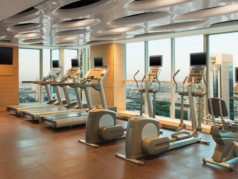 Moderner Fitnessraum mit Laufbändern, Crosstrainern und großem Fenster mit Stadtblick.