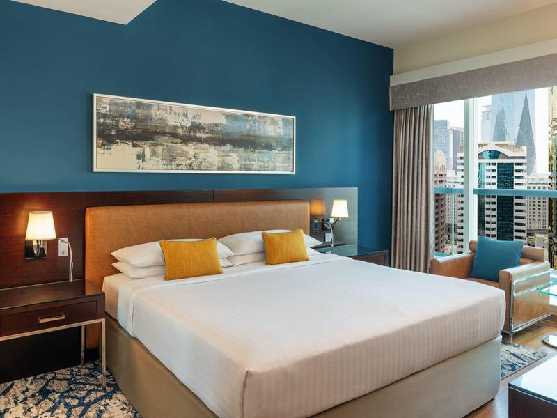 Modern eingerichtetes Hotelzimmer mit großem Bett, blauer Wand und Stadtblick vom Balkon.