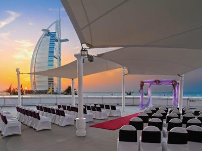 Freiluft-Hochzeitsort mit weißen Stühlen, rotem Teppich und Burj Al Arab im Hintergrund bei Sonnenuntergang.