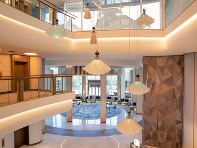 Hell beleuchteter, moderner Lobbybereich mit eleganten Treppen, Holzvertäfelung und Designerlampen.