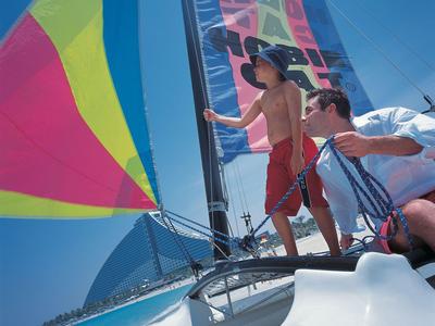 Zwei Männer segeln bei klarem Himmel auf einem Boot mit buntem Segel.