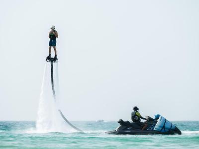 Person fliegt mit Flyboard über dem Meer, begleitet von Jet-Ski-Fahrer.