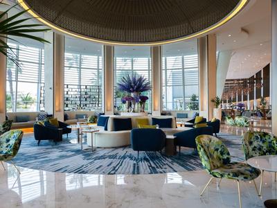 Großer, heller Hotel-Lobbybereich mit modernen Sesseln, Teppich, Pflanzen und großen Panoramafenstern.