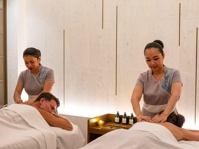 Zwei Frauen massieren in hellem Raum entspannt zwei Personen auf Massageliegen.