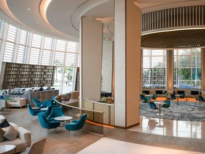 Heller, moderner Lobbybereich mit blauen Sesseln, großen Fenstern und hellen, runden Deckenformen.