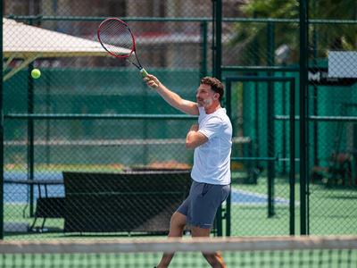 Ein Mann spielt Tennis auf einem Außenplatz bei Tageslicht.