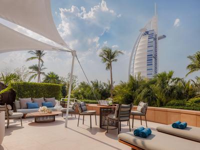 Elegante Hotelterrasse mit Liegen, Sitzbereichen und Blick auf das Burj Al Arab bei Sonnenschein.