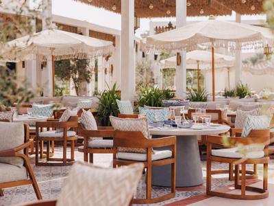 Hell eingerichteter Außenbereich eines Restaurants mit Holzmöbeln und Sonnenschirmen.