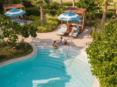 Poolbereich mit Liegestühlen, Sonnenschirmen und Gästen in tropischer Gartenanlage.